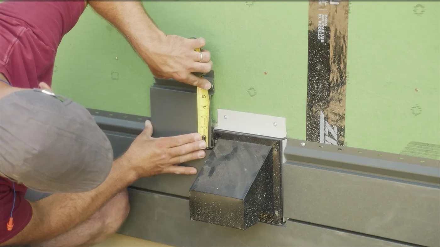Hands measuring a piece of steel siding trim against a wall